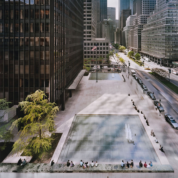 Aerial view of a downtown financial district plaza with reflecting pools, fountains, and people seated along the ledges between high-rise buildings